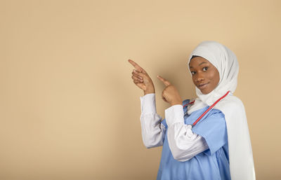 Smiling nurse in uniform and headscarf pointing fingers into empty space. advertising concept