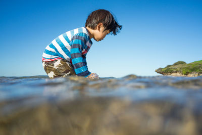 Boy playing in lake against clear blue sky