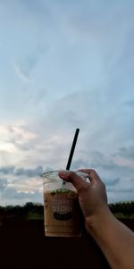 Close-up of hand holding ice cream against sky