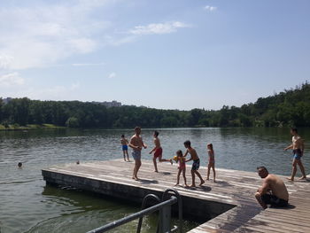 People by lake against sky