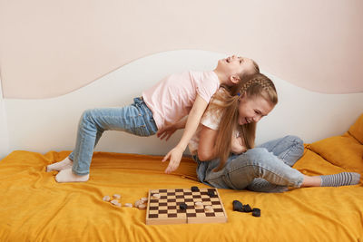 Sisters playing draughts board game on bed