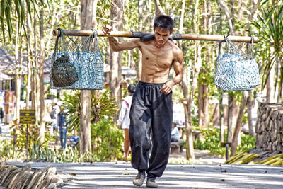 Full length of shirtless man standing against plants