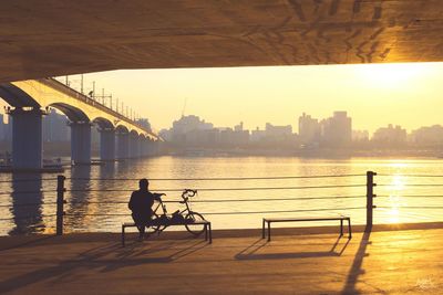 Silhouette of men on bridge over river in city