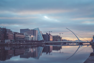 River by illuminated city against sky during sunset