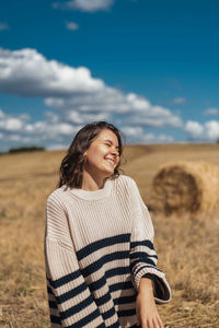 Smiling young woman standing on field against sky