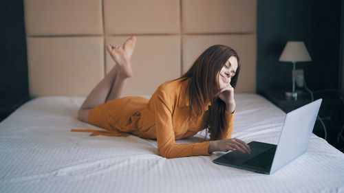 Full length of woman lying on bed and using laptop