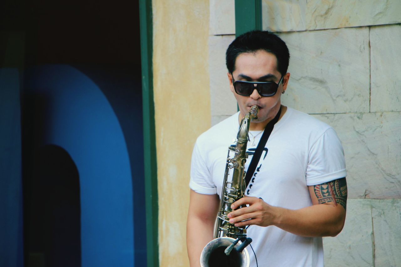 one person, young men, real people, music, young adult, musical instrument, lifestyles, saxophone, artist, standing, glasses, musician, men, holding, leisure activity, casual clothing, playing, architecture, arts culture and entertainment