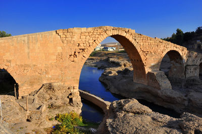 Arch bridge over rocks against blue sky