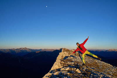 Man on rock against clear blue sky