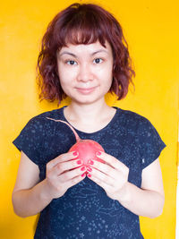 Portrait of woman holding radish against yellow background