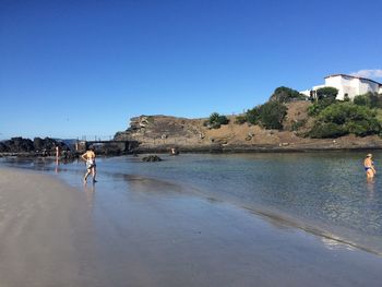 People at beach against clear blue sky