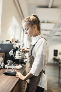 Side view of young female barista making coffee at counter