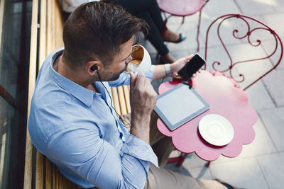 High angle view of businessman drinking coffee while using smart phone at sidewalk cafe