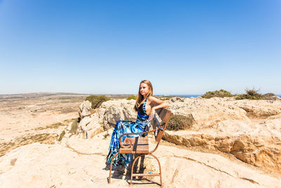 Woman sitting on rock against clear blue sky