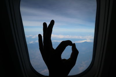 Close-up of silhouette hand gesturing against airplane window