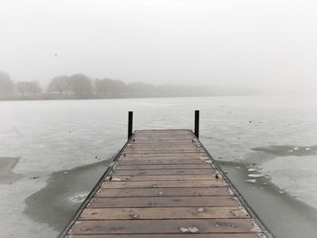 Pier on frozen lake against sky during winter