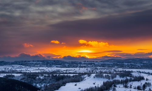 Snow covered landscape against sky during sunset