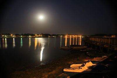Illuminated city by sea against sky at night