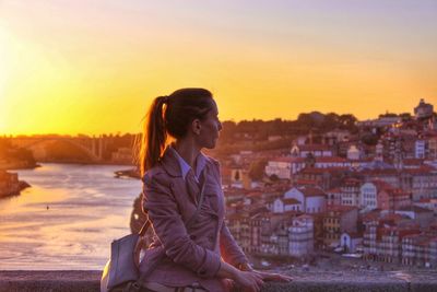 Side view of man standing by cityscape against sky during sunset