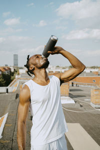 Young man drinking water from bottle on rooftop during sunny day