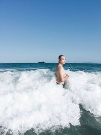 Full length of shirtless man in sea against clear sky