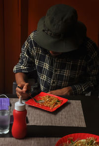 A bearded and long haired young man eating noodles in the restaurant during covid-19 pandemic.