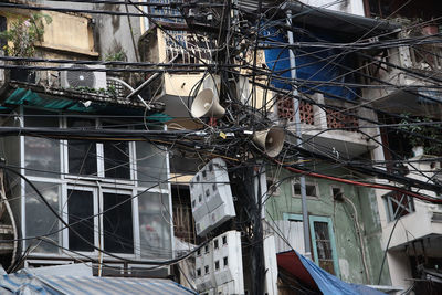 Low angle view of tangled on cables on pole against building