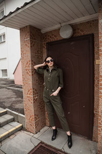 Full length front view portrait of tall slim brunette in green suit in urban setting, fashion  