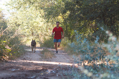 Man running with dog on footpath in forest