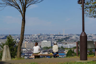 Rear view of men sitting on bench against cityscape