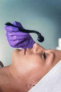 Close-up of woman lying down with while beautician using cosmetic roller on face at spa