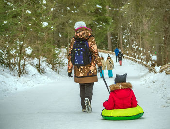 Mom is towing kite tube with a her son on the snow. towed snow tubing. rear view.