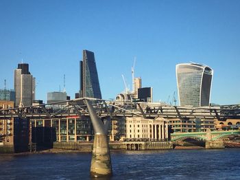 Modern buildings by river against clear blue sky