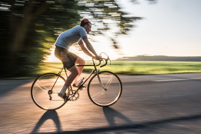 Blurred motion of man riding bicycle on road during sunny day