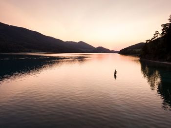 Man standing in lake against sky during sunset