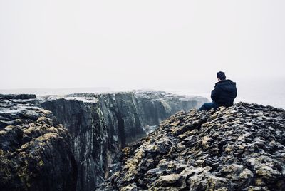 Rear view of man sitting on rock against sky