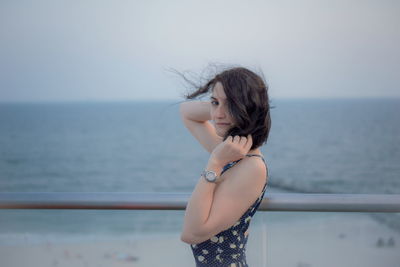 Side view portrait of beautiful woman standing by sea against sky