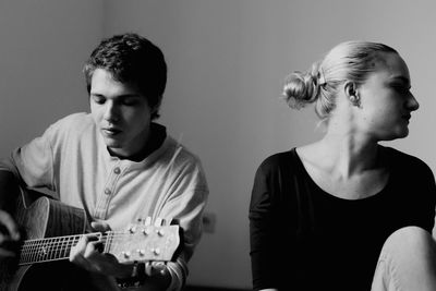 Young man with guitar by friend sitting at home