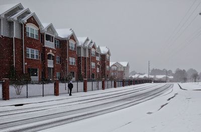 Snow covered road by buildings against sky