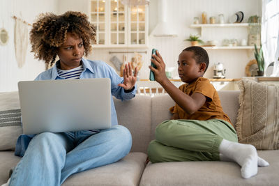 Annoyed mother working on laptop asking child not to disturb her