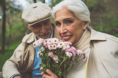 Portrait of senior woman with husband holding flower at park