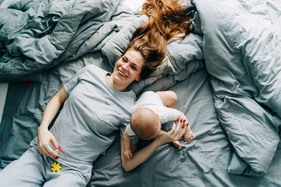 Young happy beautiful mother with baby lies in bed, top view