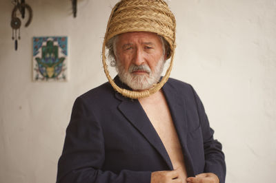 Portrait of man wearing basket on head while standing against wall