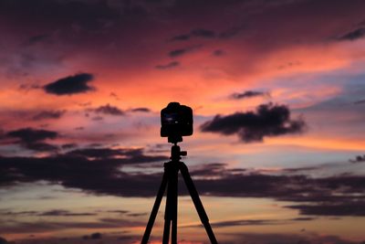 Silhouette of camera against sky during sunset