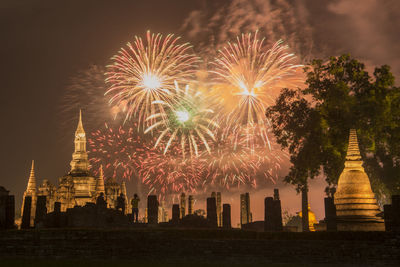 Firework display over building against sky at night