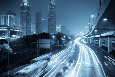 Light trails on road amidst buildings against sky at night