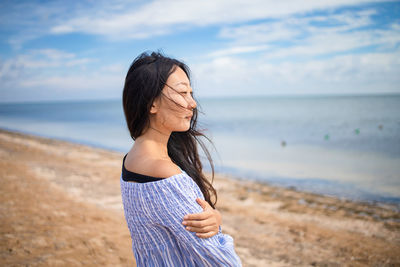 Young woman standing at beach against sky