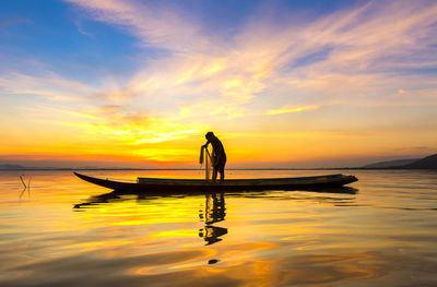 Silhouette man standing on boat in sea against sky during sunset