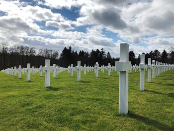 Panoramic low angle view of white crosses in cemetery against cloudy sky