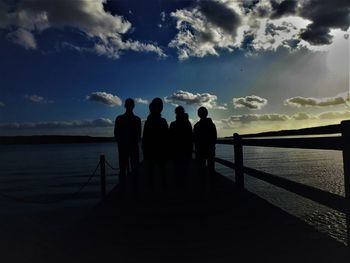 Silhouette people standing on pier over sea during sunset